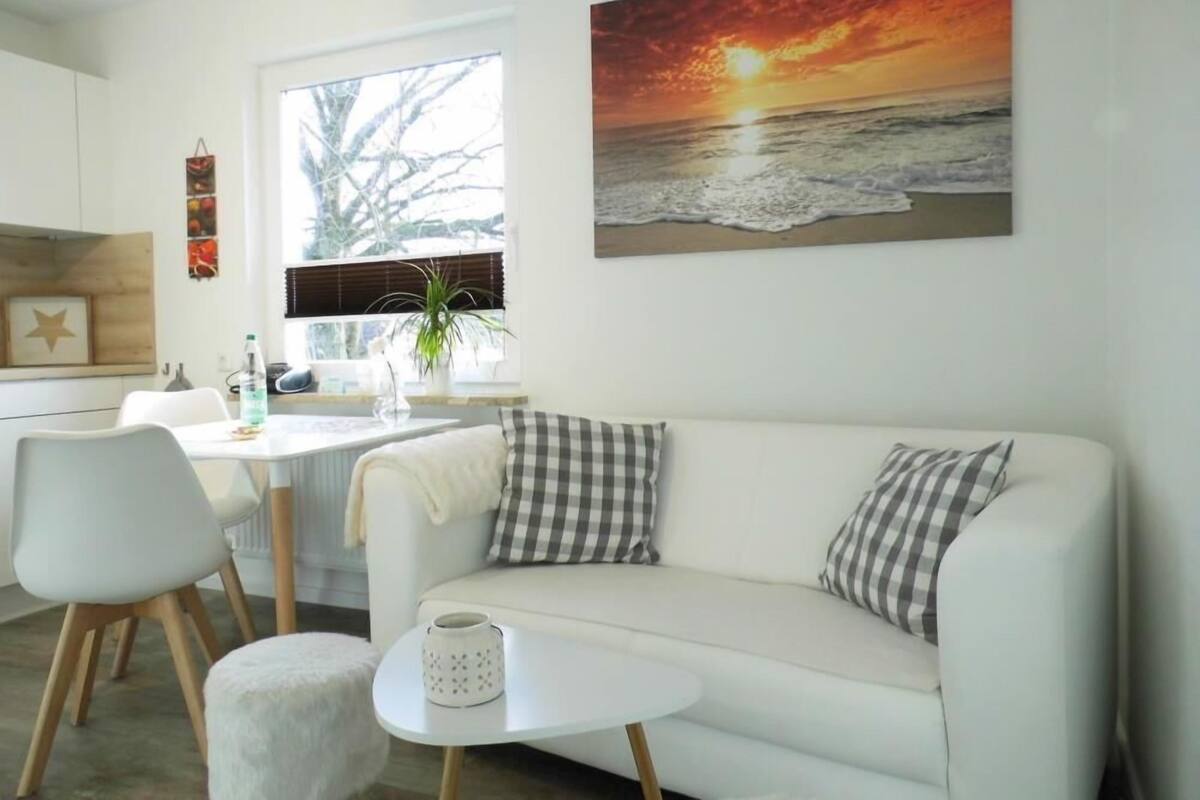 A modern living room with a white sofa, a small round table, and a painting of a sunset over the ocean.