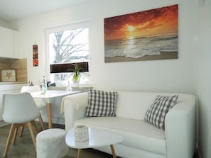 A modern living room with a white sofa, a small round table, and a painting of a sunset over the ocean.