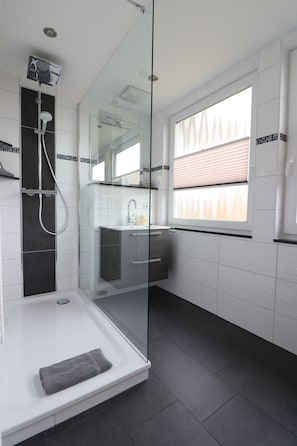 A modern bathroom with a glass-enclosed shower, a sink, and a window with blinds.