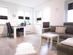 Uma sala de estar moderna com um sofá branco, uma mesa de centro e um espaço de refeições com uma mesa e cadeiras.