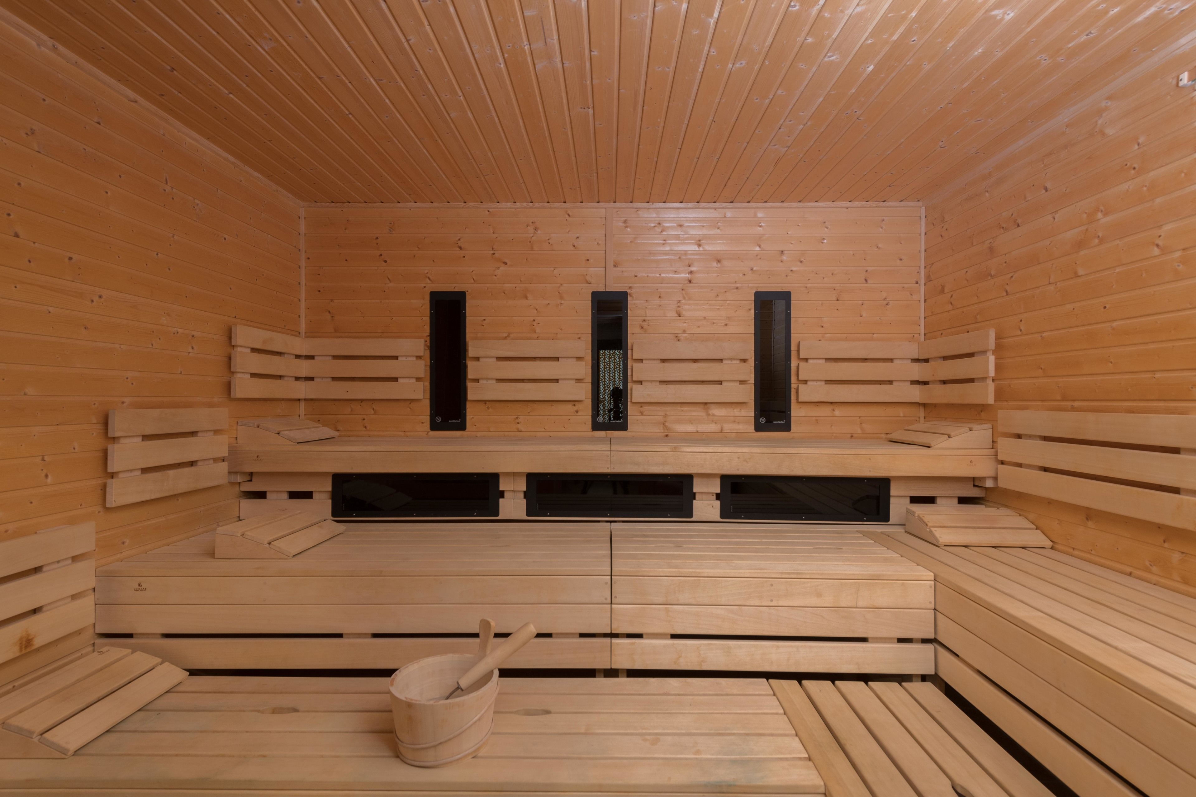 Una sauna con bancos de madera, un cubo y un calentador fijado a la pared.