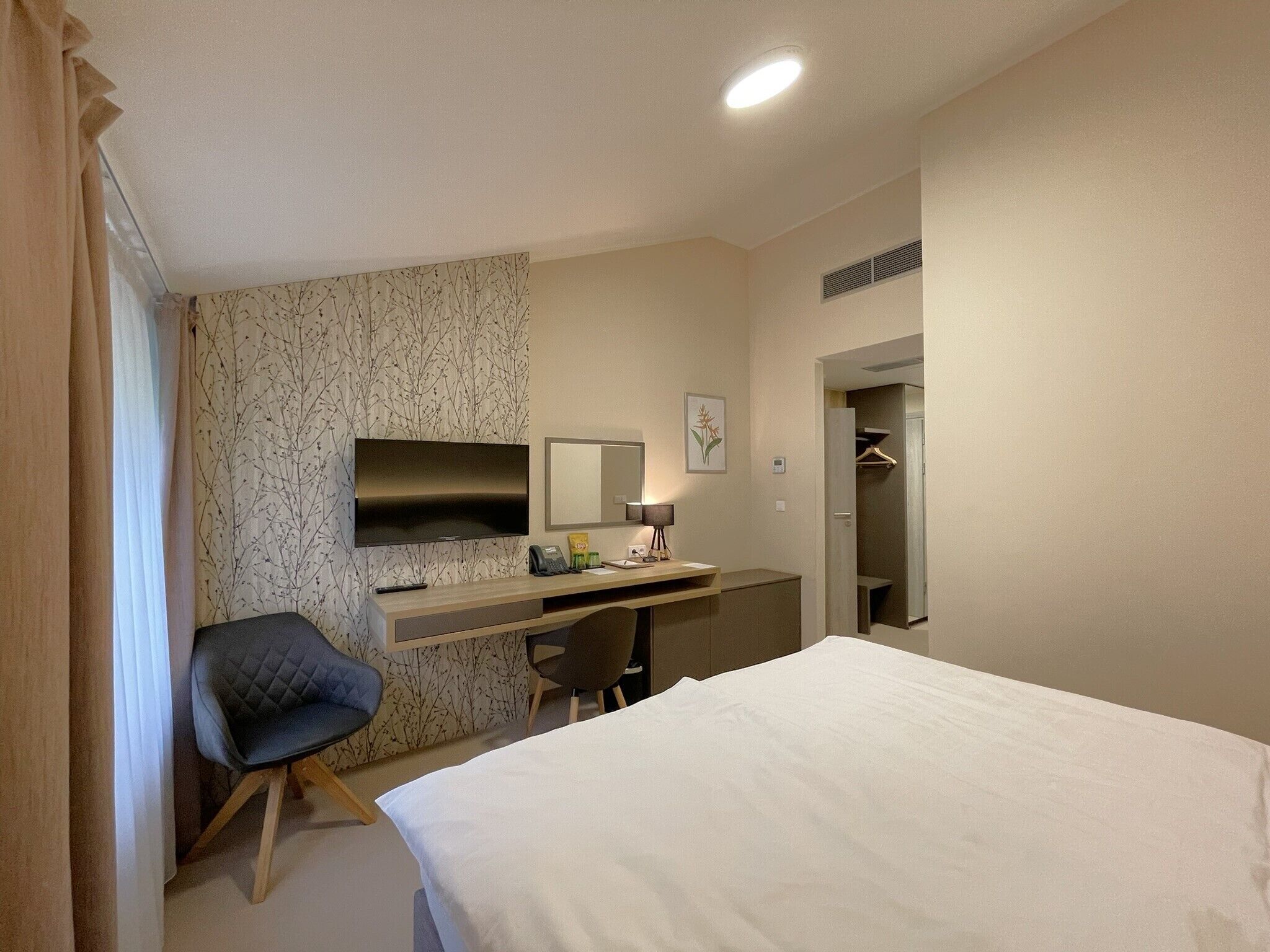 A hotel room with a bed, a desk with a chair, a television, a mirror, and a wardrobe.