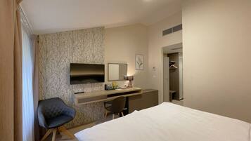A hotel room with a bed, a desk with a chair, a television, a mirror, and a wardrobe.