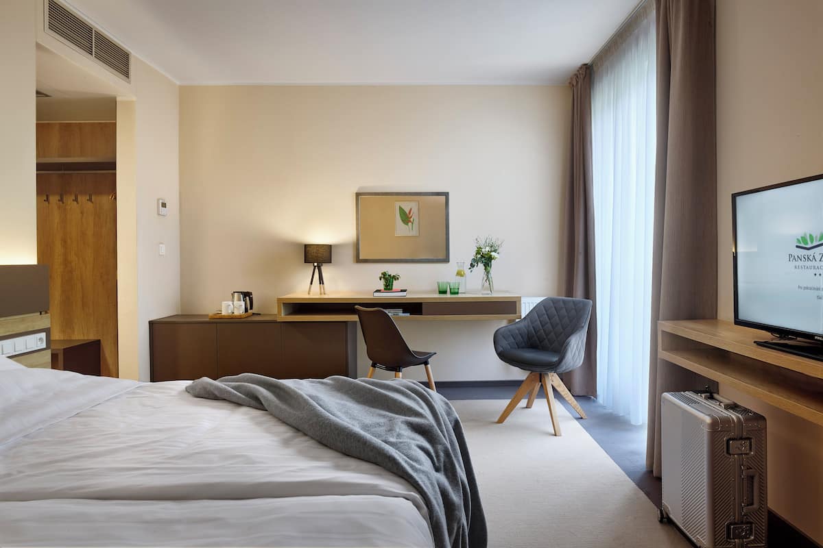A hotel room with a bed, a desk, a chair, a television, and a suitcase.