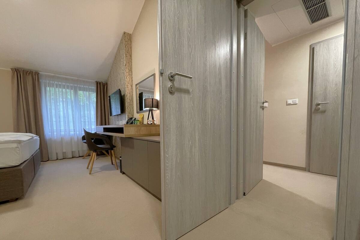 A hotel room with a bed, a desk with a chair, a TV, and a wardrobe.
