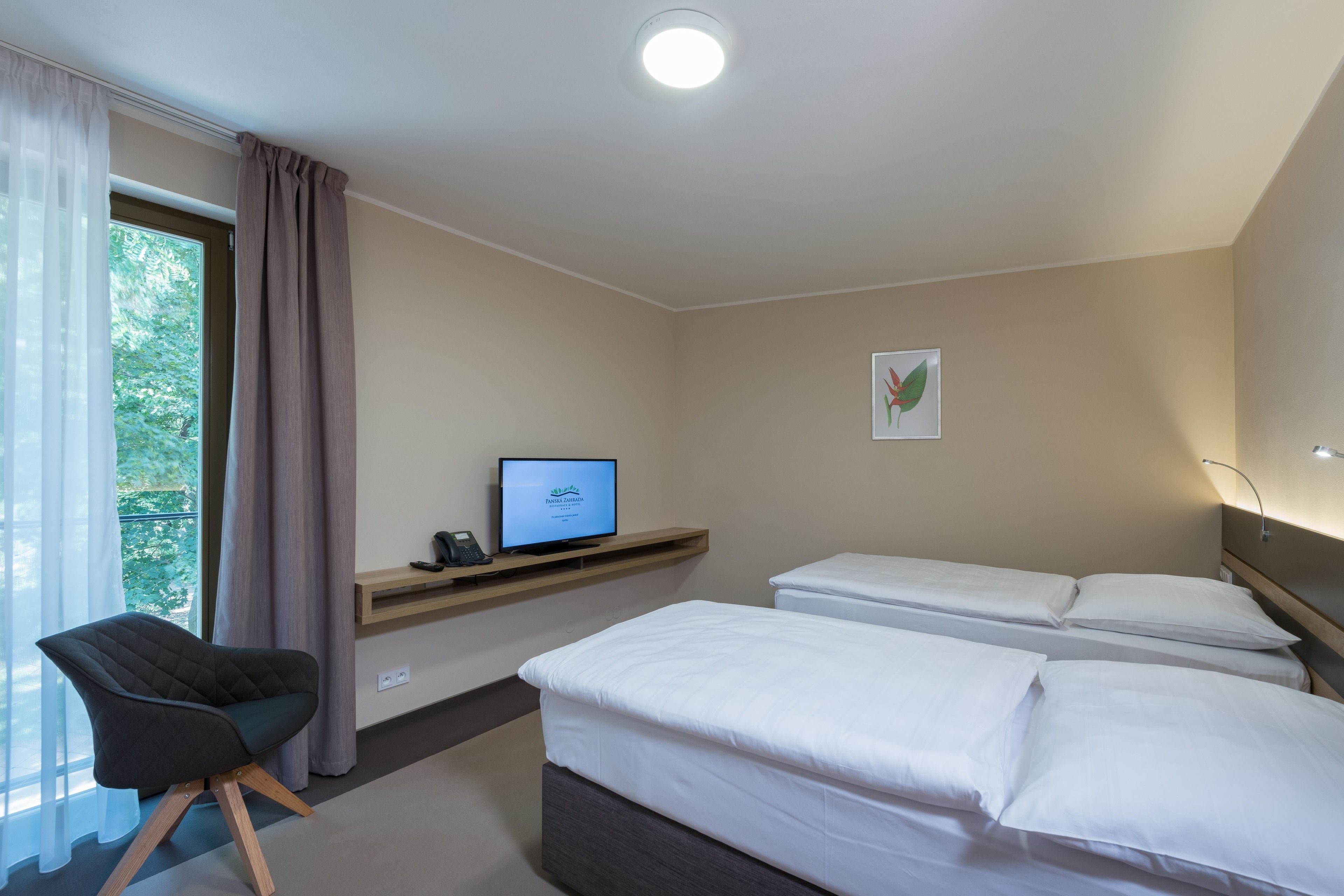A hotel room with a bed, a chair, a TV on a shelf, and a window with curtains.