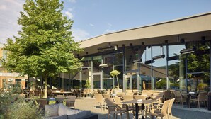 Een terras met rieten meubilair en een groot glazen gebouw op de achtergrond.