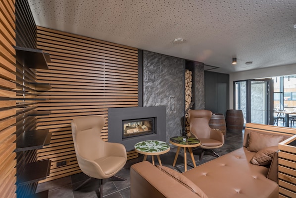 A modern interior with a fireplace, leather seating, and a stone accent wall. - Hotel Panská Zahrada (Dobrichovice)