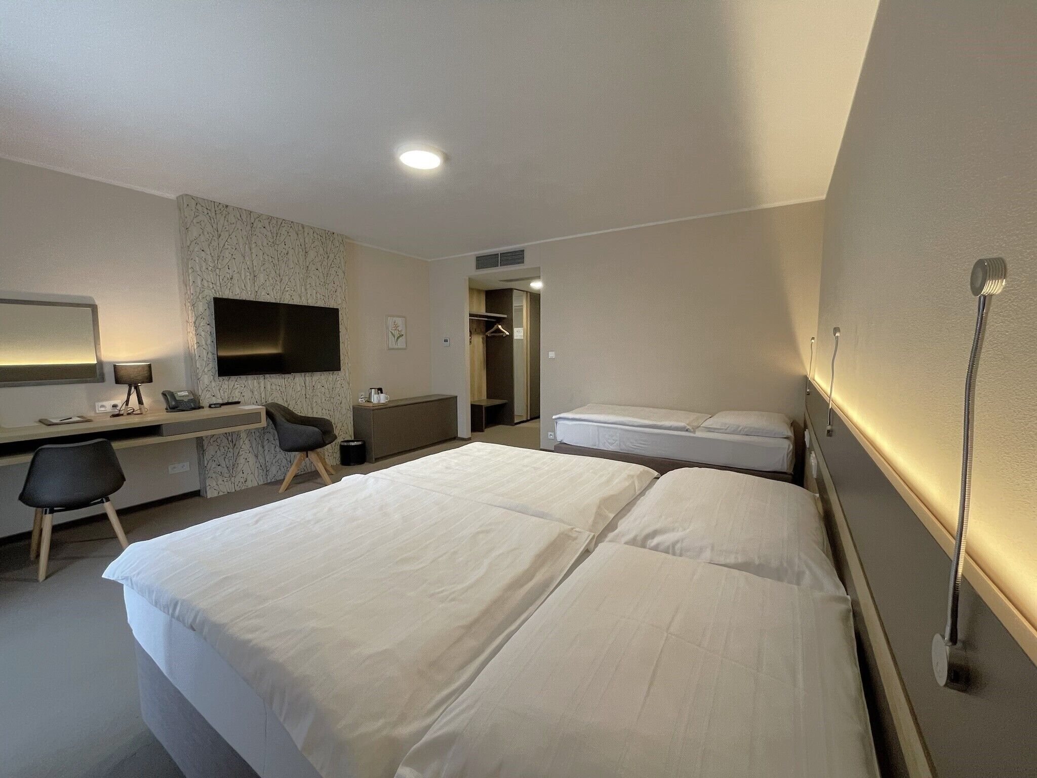 Ein Hotelzimmer mit Bett, Schreibtisch, Stuhl, Fernseher und Dusche.
