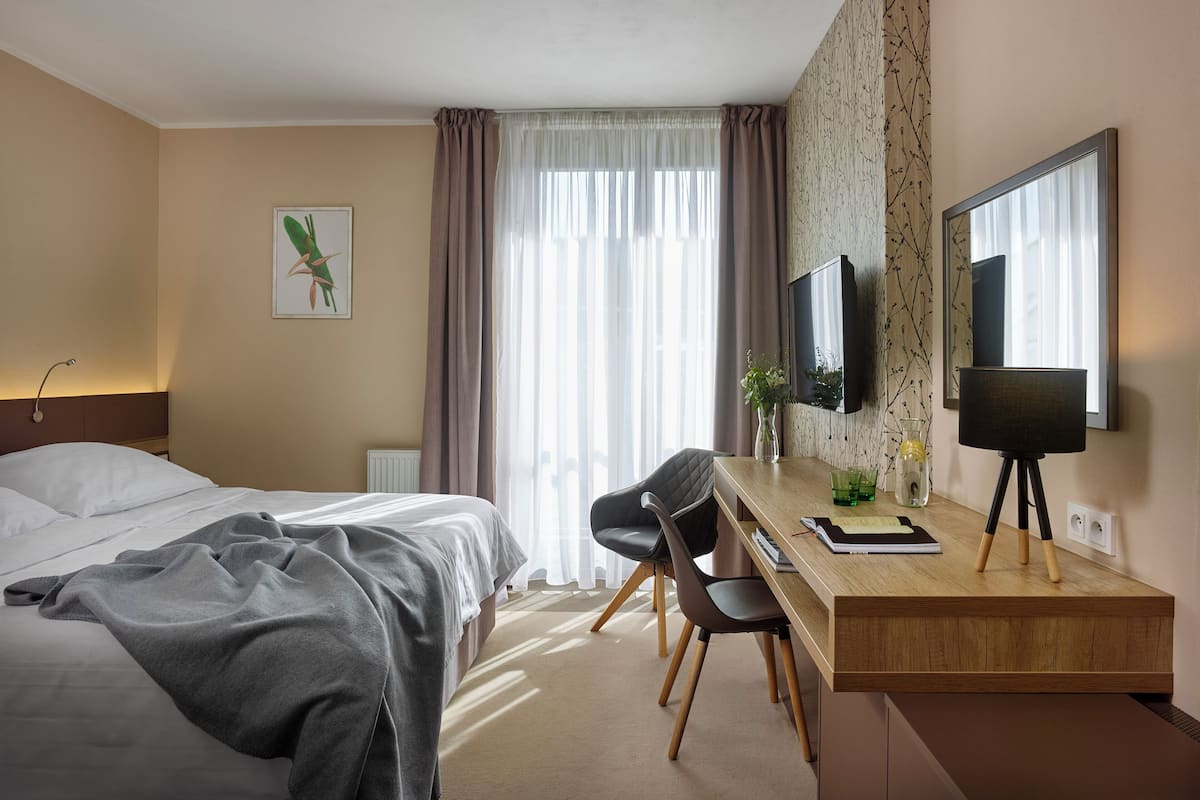 A hotel room with a bed, a desk with a chair, a TV, and a window with curtains.