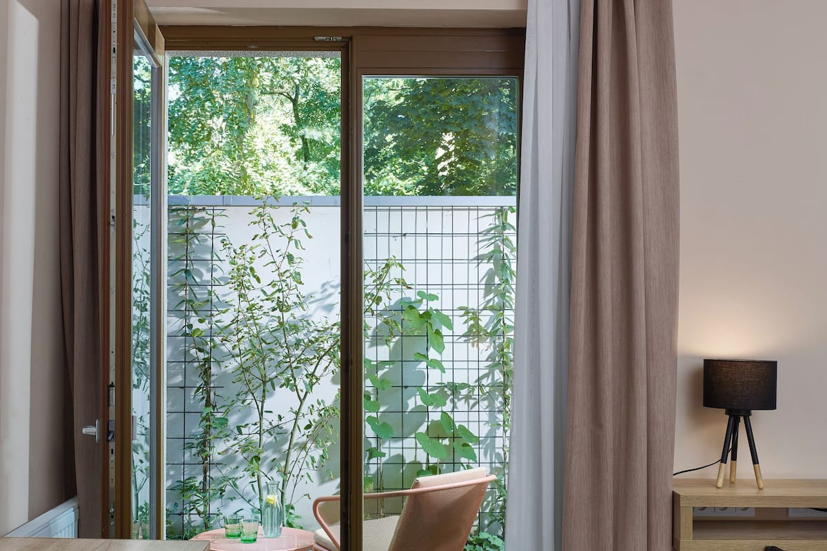 A hotel room with a desk, chair, and a view of a garden through a glass door.