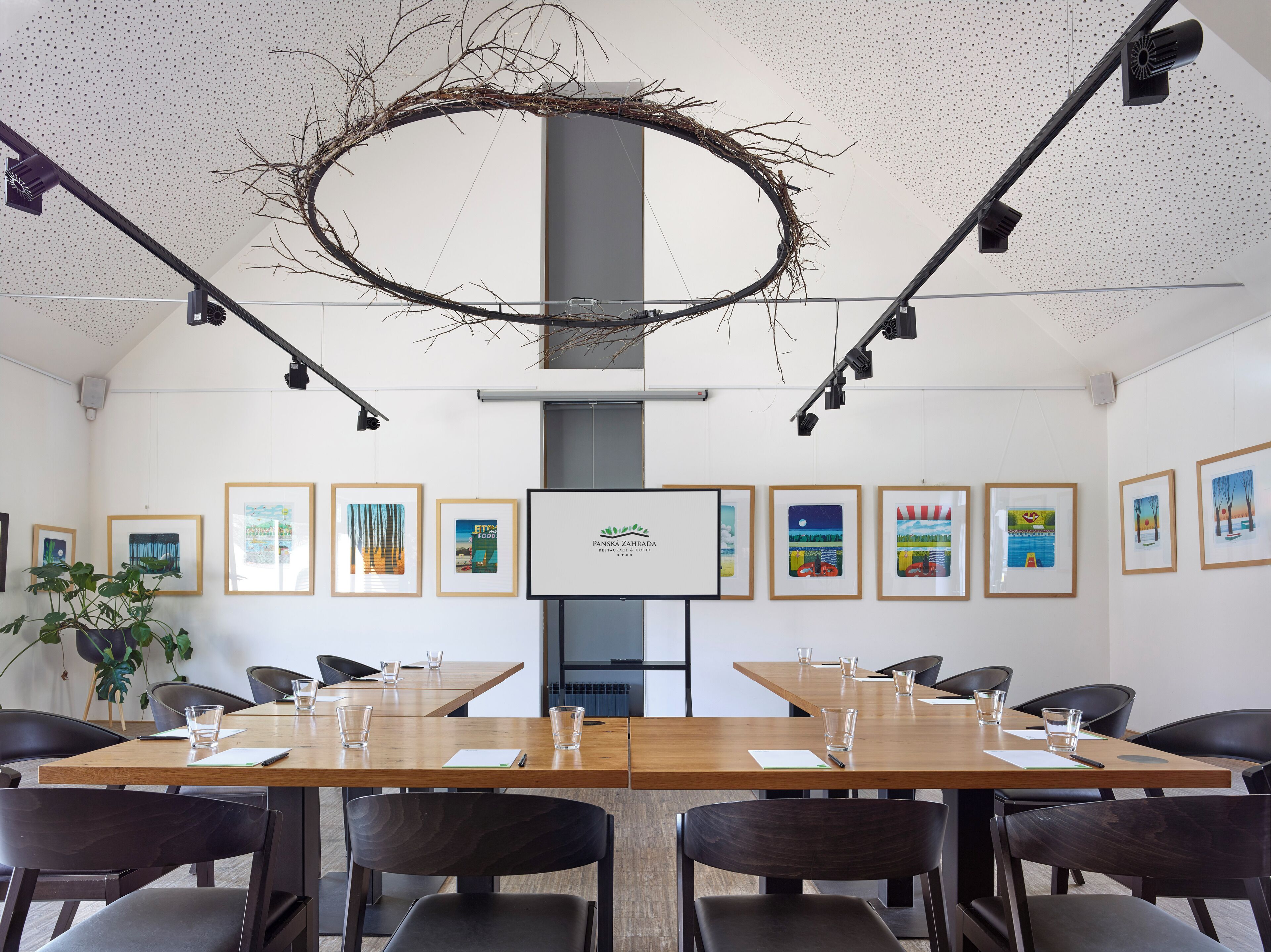 Een vergaderruimte met een lange tafel, stoelen, ingelijste foto’s aan de wanden en een logo op het scherm.
