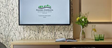 Una recepción con un monitor mostrando el nombre 'PANSKÁ ZAHRADA RESTAURACE & HOTEL' y un fondo de papel tapiz floral.