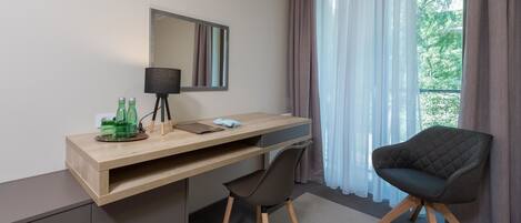 Una habitación moderna con un escritorio de madera, una silla negra, un espejo y una ventana con cortinas.