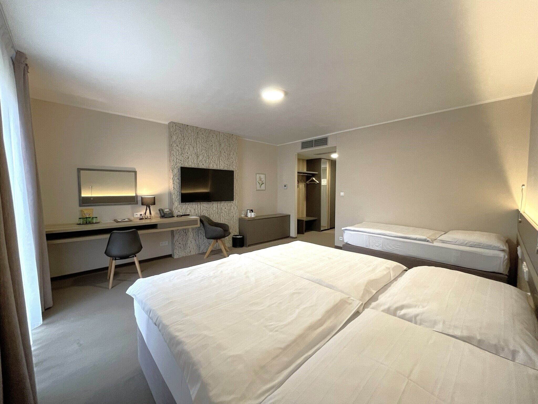 A hotel room with two beds, a desk, a chair, a TV, and a wardrobe.