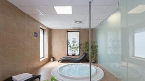Een wellnessruimte met een jacuzzi, een massagestoel en een klein tafeltje met glazen.
