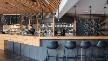 Un bar moderno con mostrador de madera, taburetes negros y una pizarra con la carta.