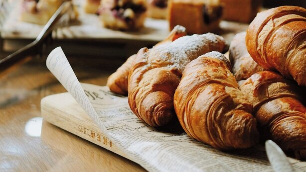 A breakfast table with croissants, a glass of orange juice, and a newspaper.