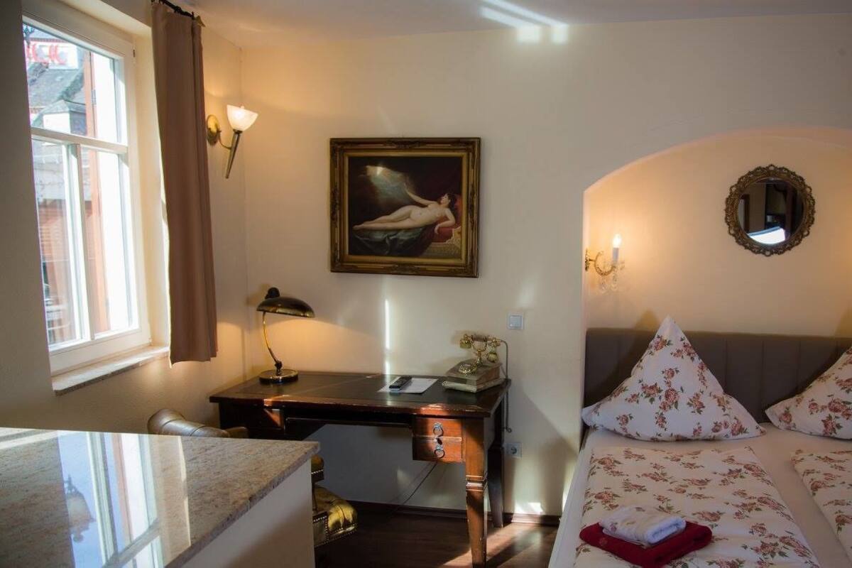 A room with a bed, a desk, a lamp, a painting, and a mirror.