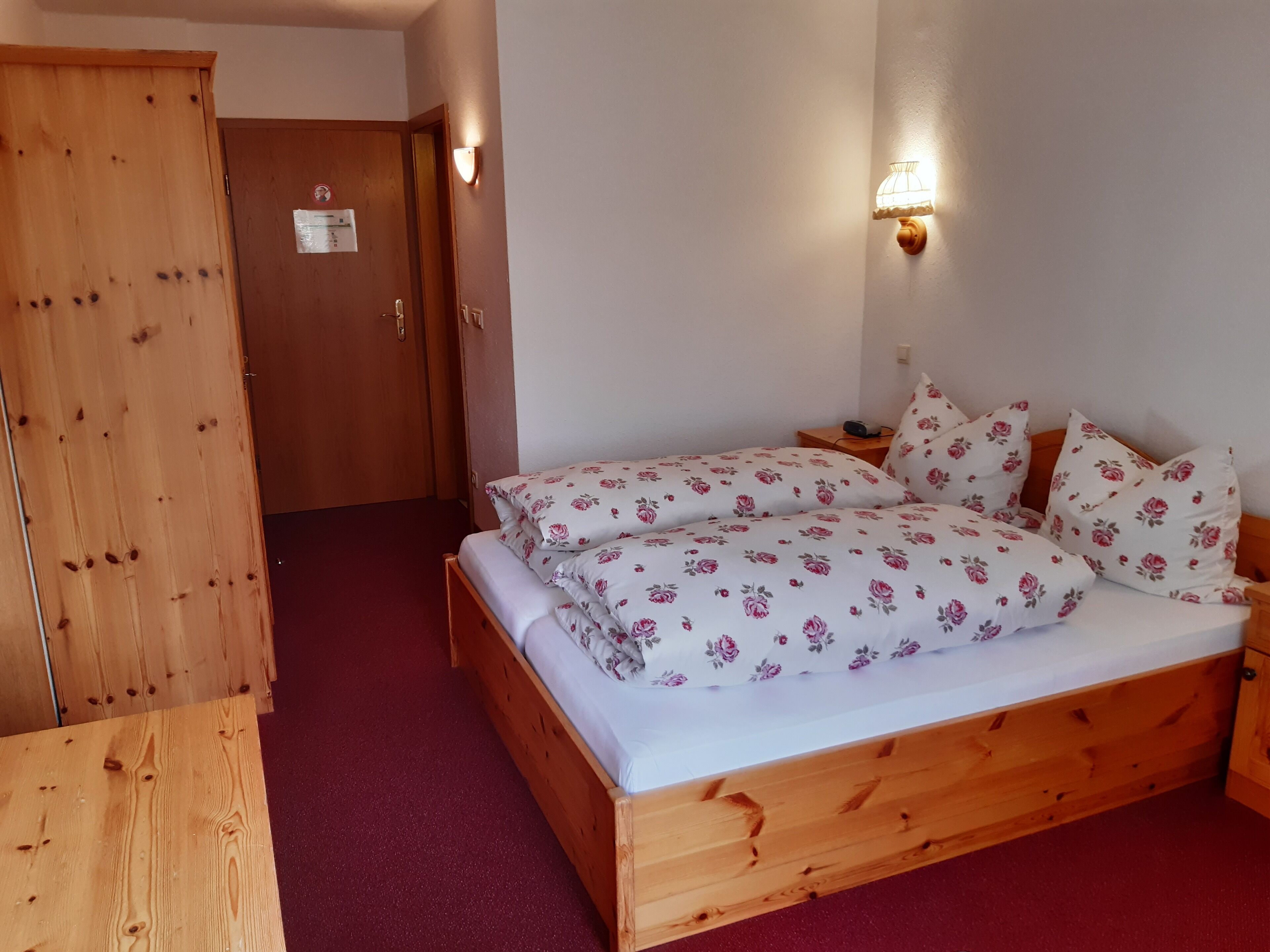 A wooden bed with floral bedding, a nightstand, and a wall-mounted light fixture.