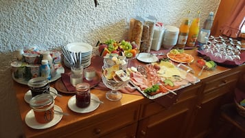 A buffet table with various food items, including fruits, cheeses, and meats, along with condiments and beverages.