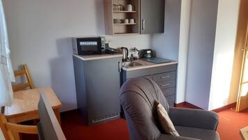 A compact kitchenette with a microwave, kettle, and sink. There is a chair and a small table in the room.