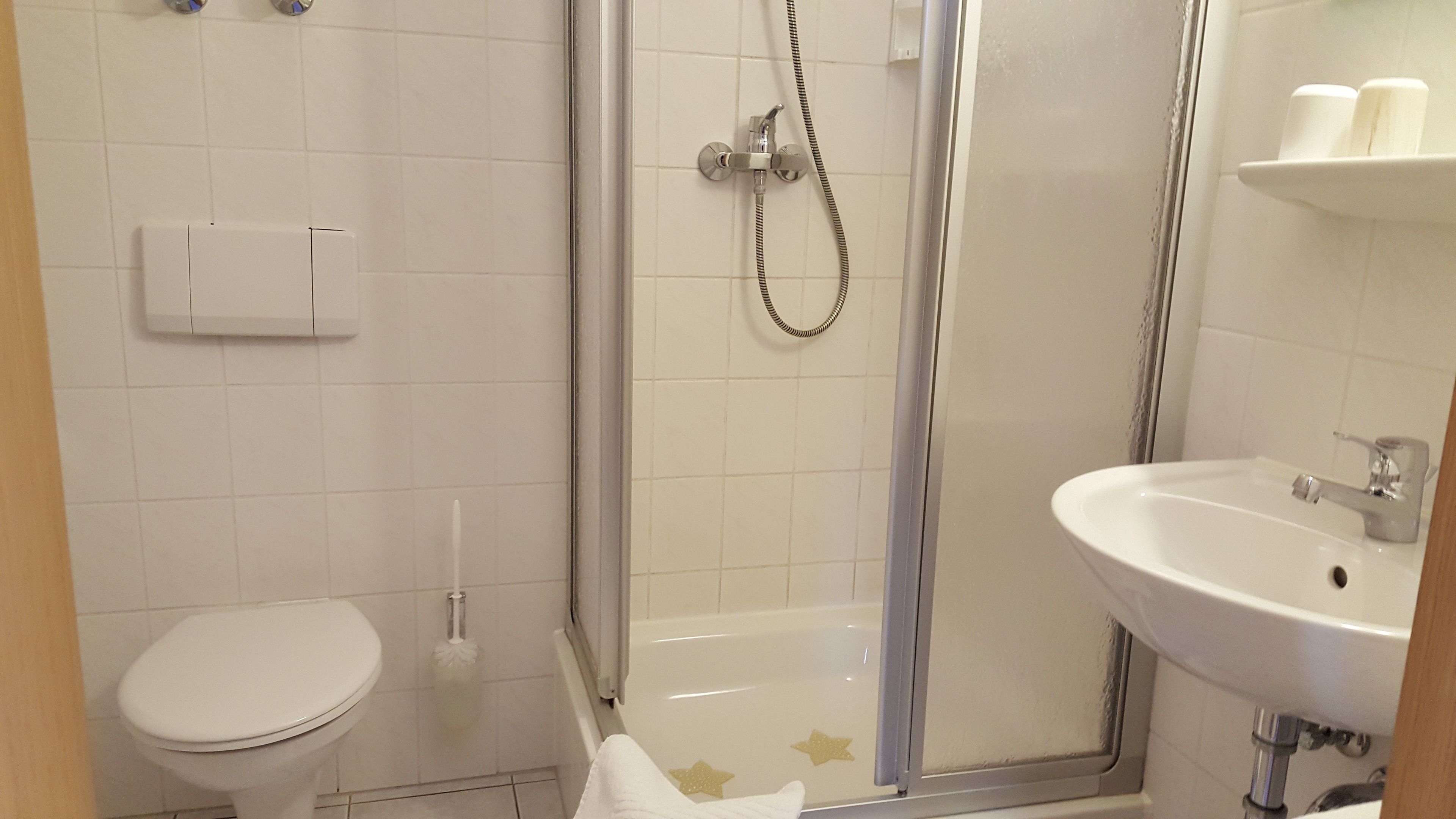 Et badeværelse med toilet, bruser med glasdør og håndvask.