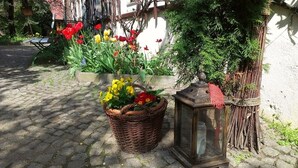 En gång belagd med kullersten, en flätkorg fylld med blommor, en lykta och ett trästaket.