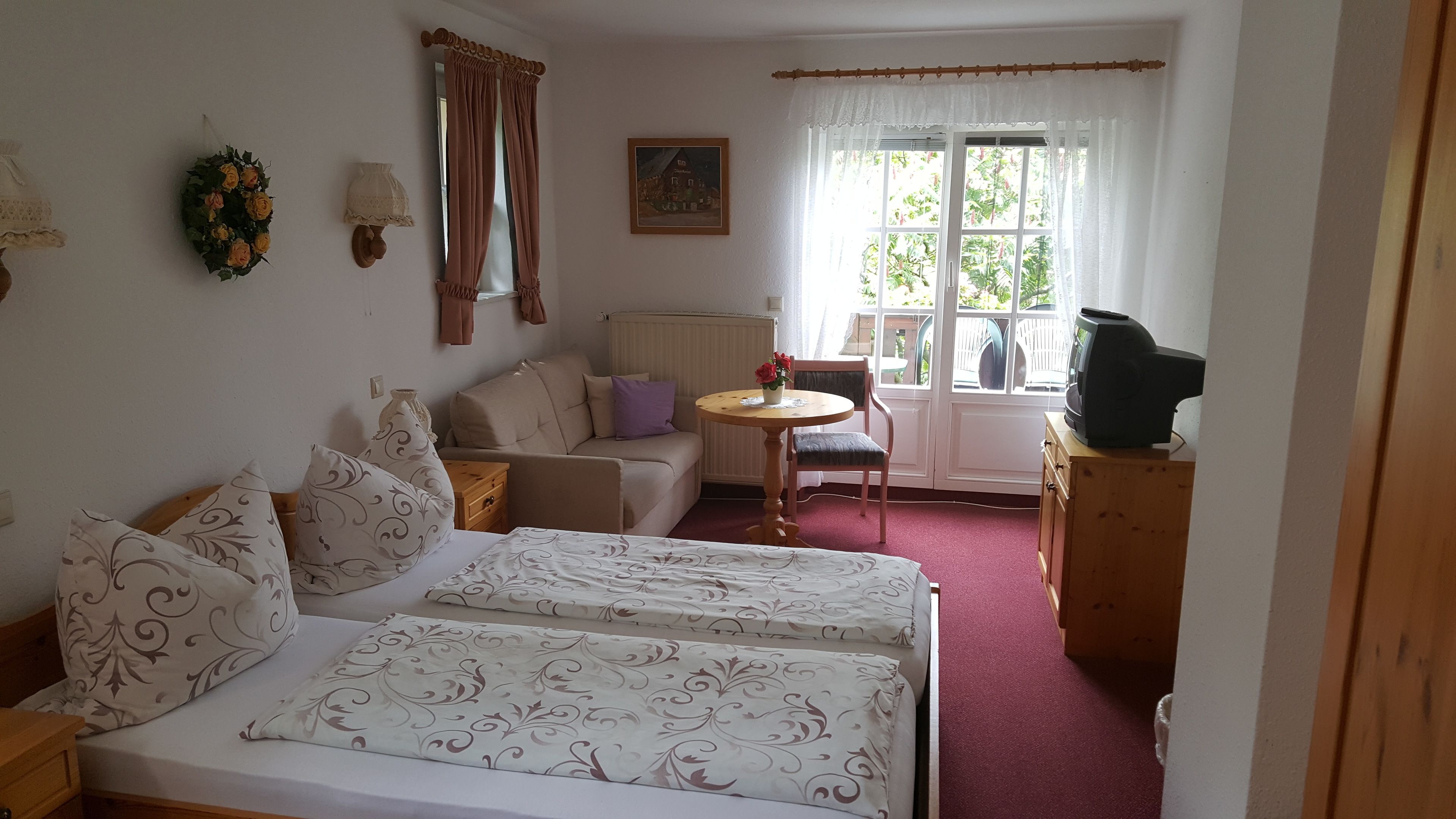 Une chambre avec deux lits, un canapé, une petite table, un téléviseur et une fenêtre avec des rideaux.