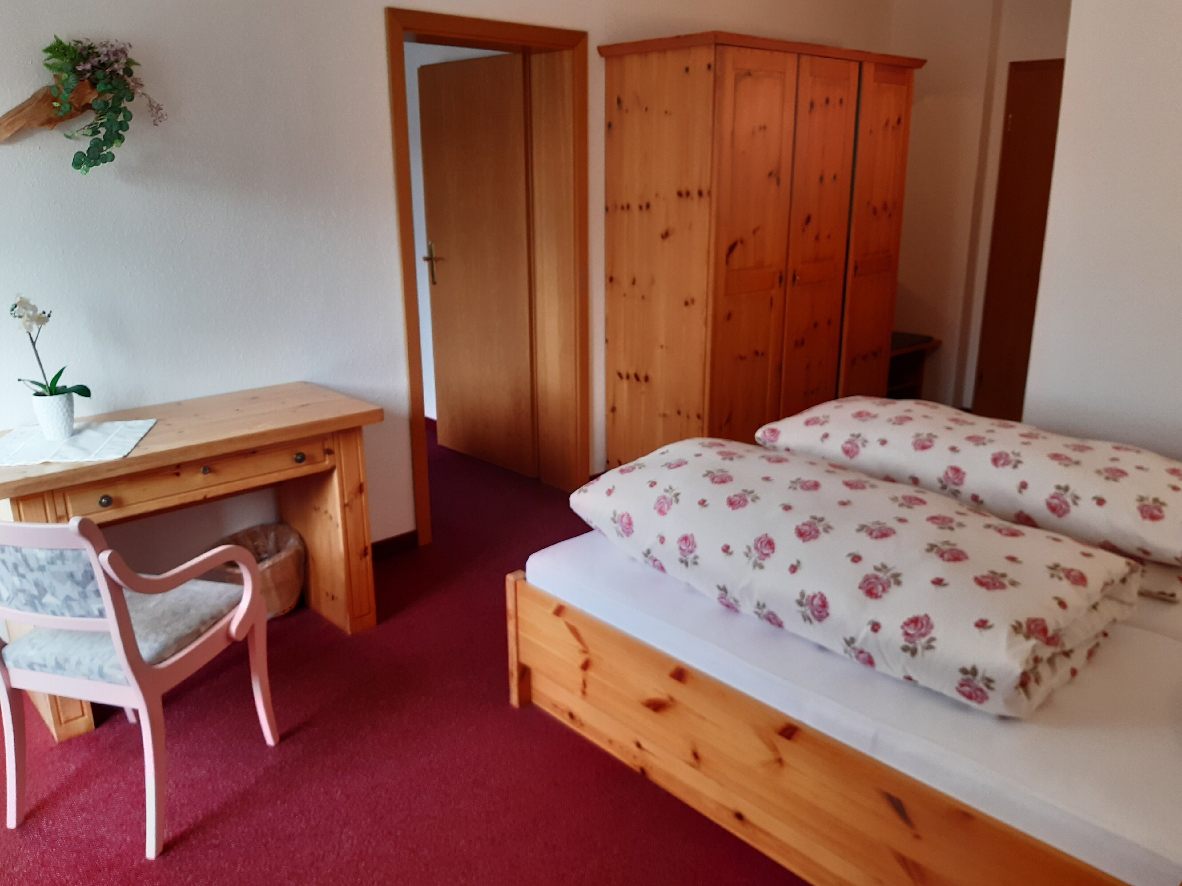 Una camera da letto con un letto di legno, una scrivania con una sedia, un armadio e una piccola pianta appesa al muro.