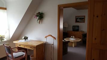A room with a wooden desk, a chair, a small table with a vase, a television, and a cabinet.