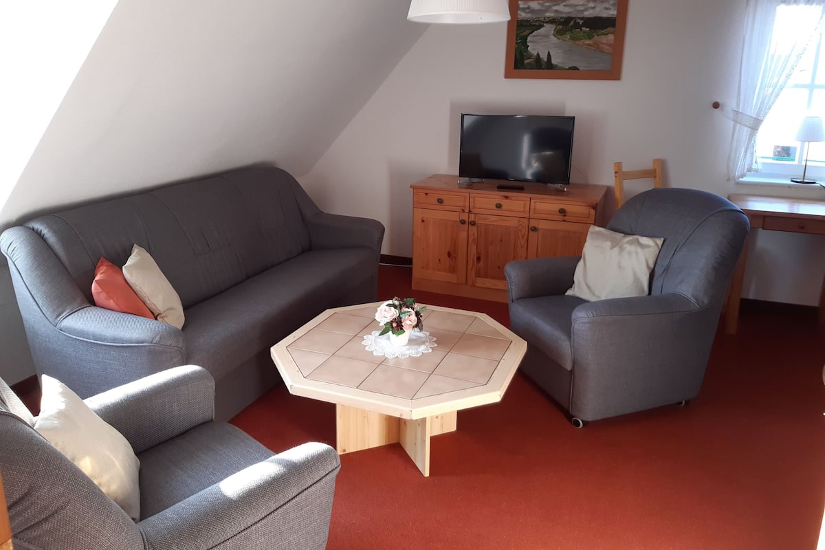 A living room with a gray sofa, a gray armchair, a wooden coffee table, and a TV on a wooden cabinet.