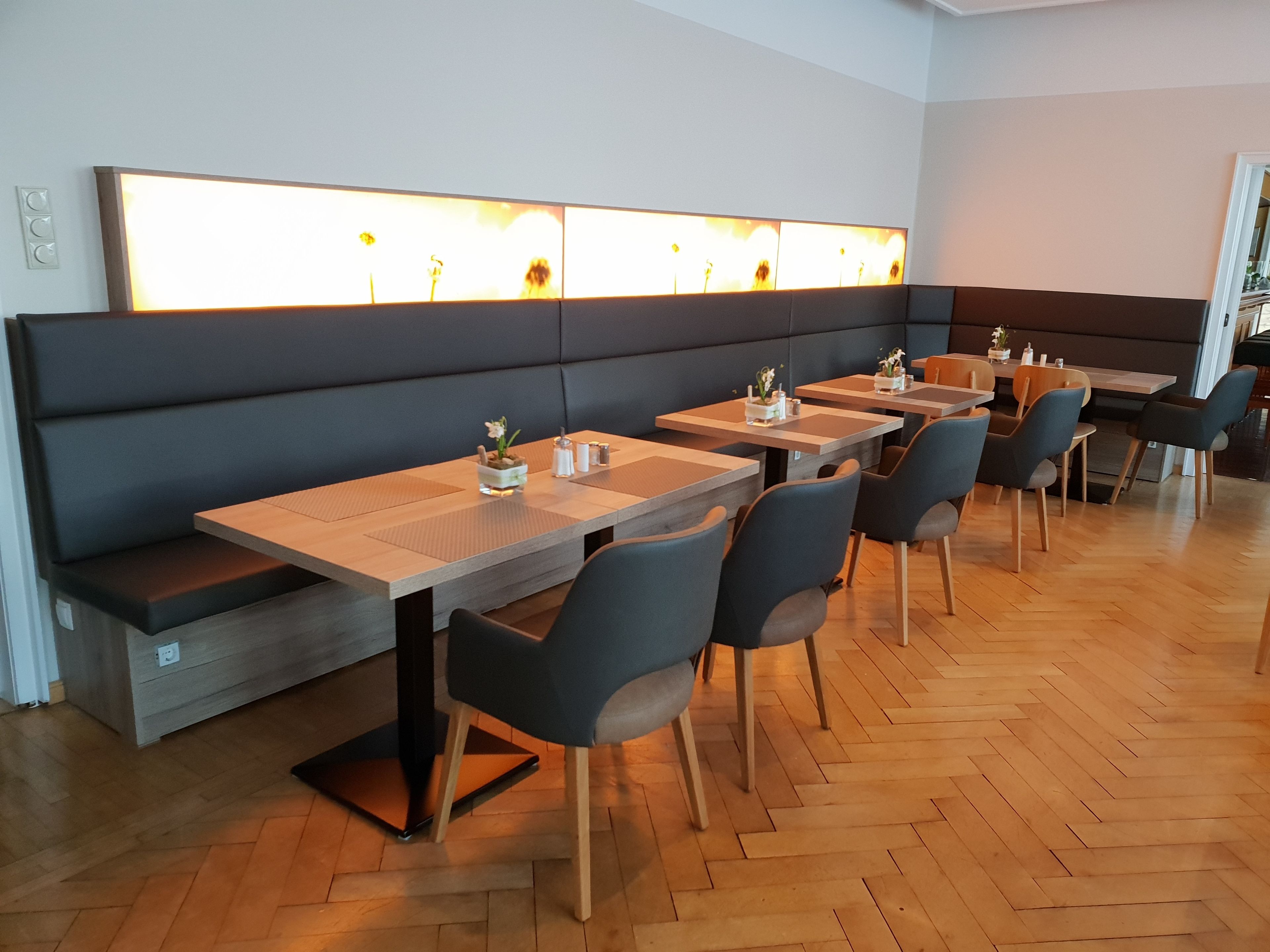 Ein modernes Restaurant mit Holztischen und schwarzen Sitzbänken.
