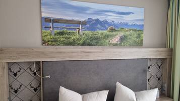 Habitación de hotel con cama, dos almohadas, un cuadro colgado de un paisaje montañoso y cabecera de madera.