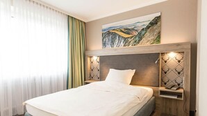 Una habitación de hotel con una cama grande, un cabecero con un panel decorativo, una mesita de noche con una lámpara y un cuadro sobre la cama.