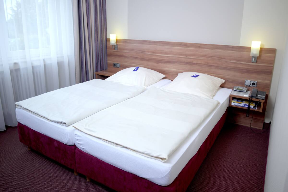 A double bed with a wooden headboard, two bedside tables with lamps, and a window with sheer curtains.