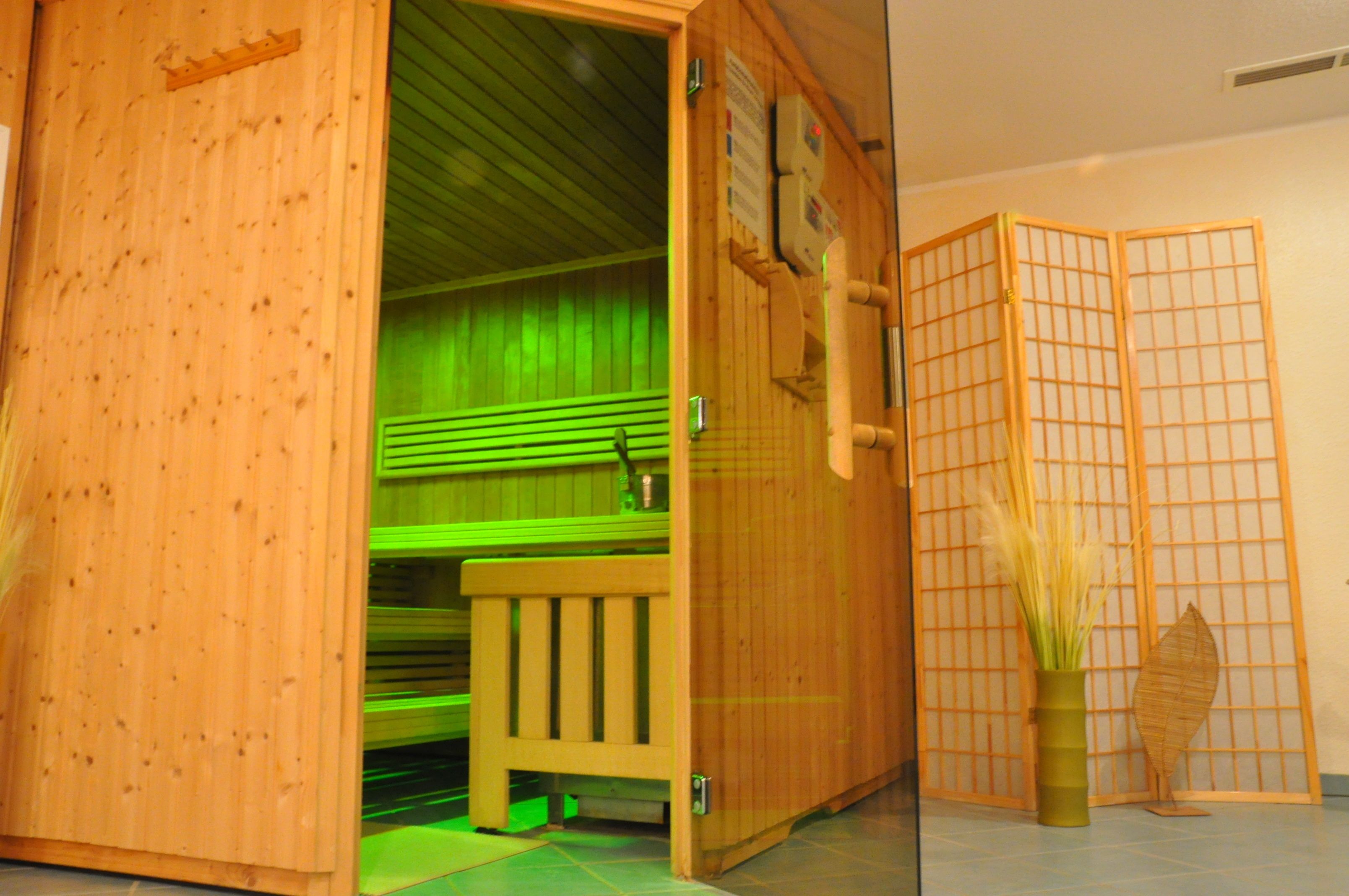 Una sauna de fusta amb una banca i una cortina verda, una separació de fusta i un ram de plantes seques.