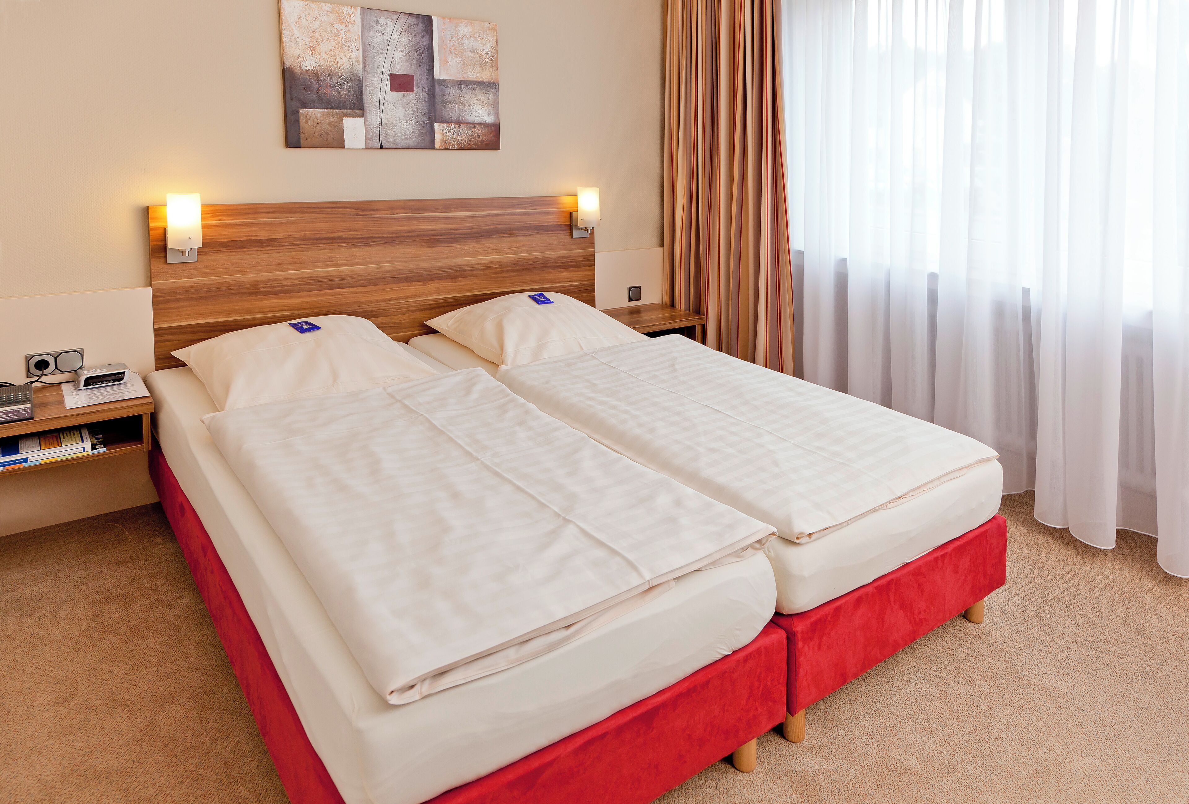 A double bed with a wooden headboard, a bedside table with a lamp, and a wall-mounted artwork.