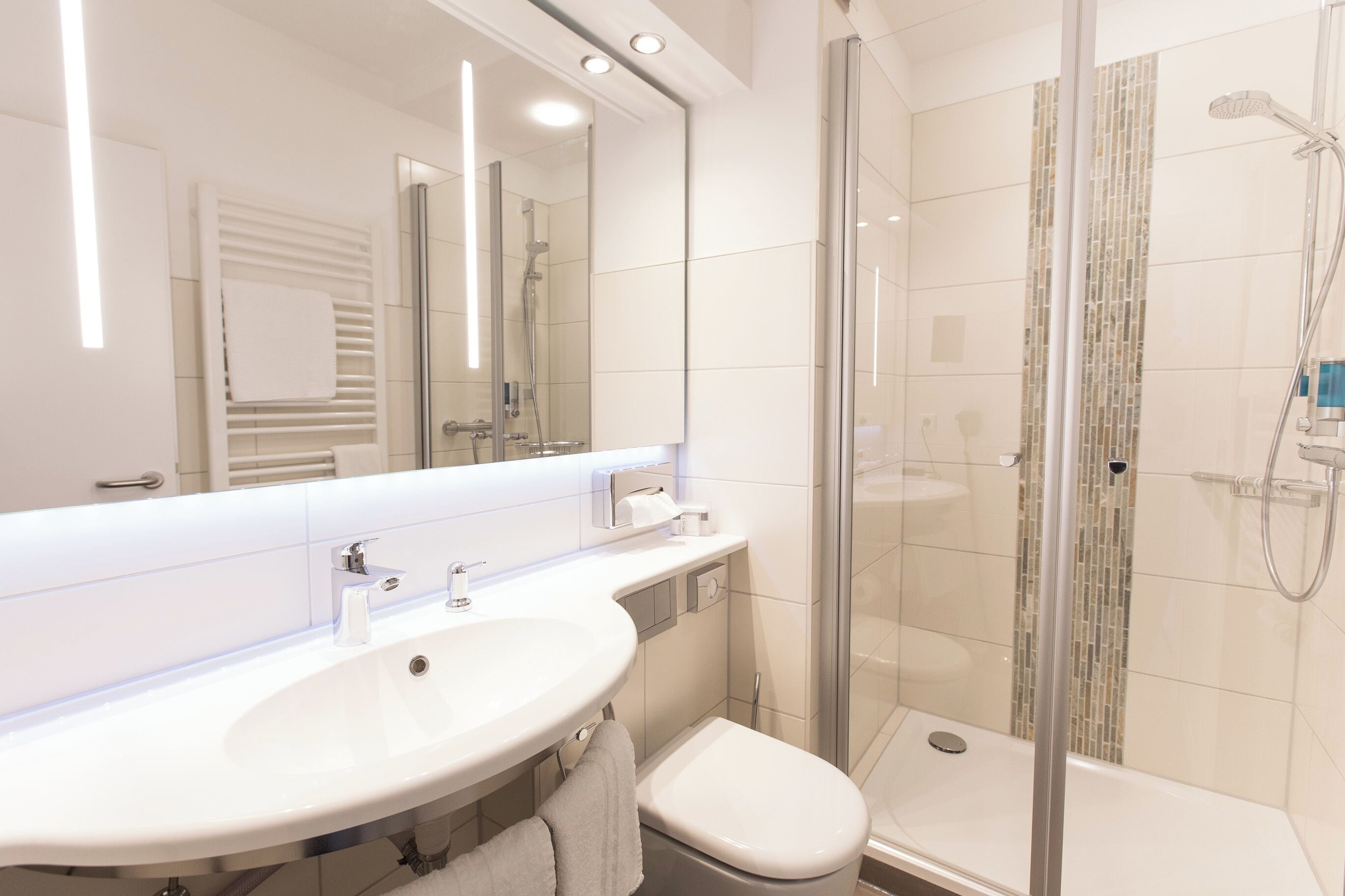 Un baño moderno con lavamanos, espejo y ducha blancos.