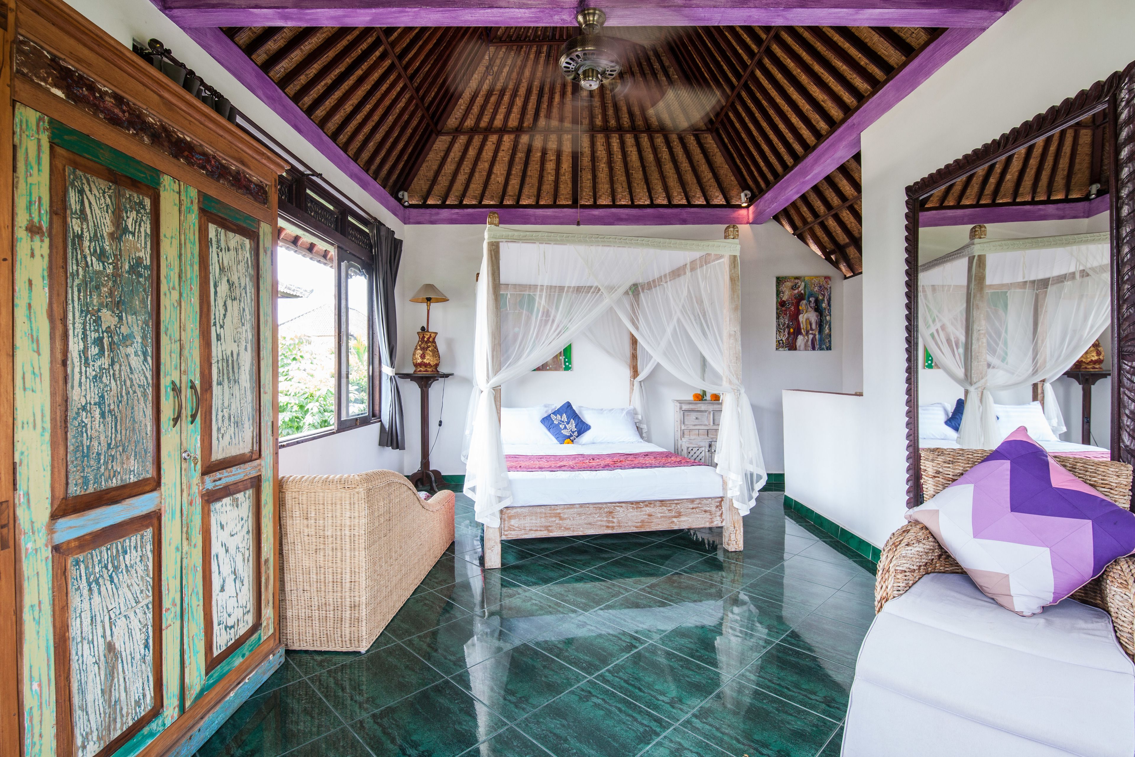 A room with a four-poster bed, a wicker sofa, and a large mirror.