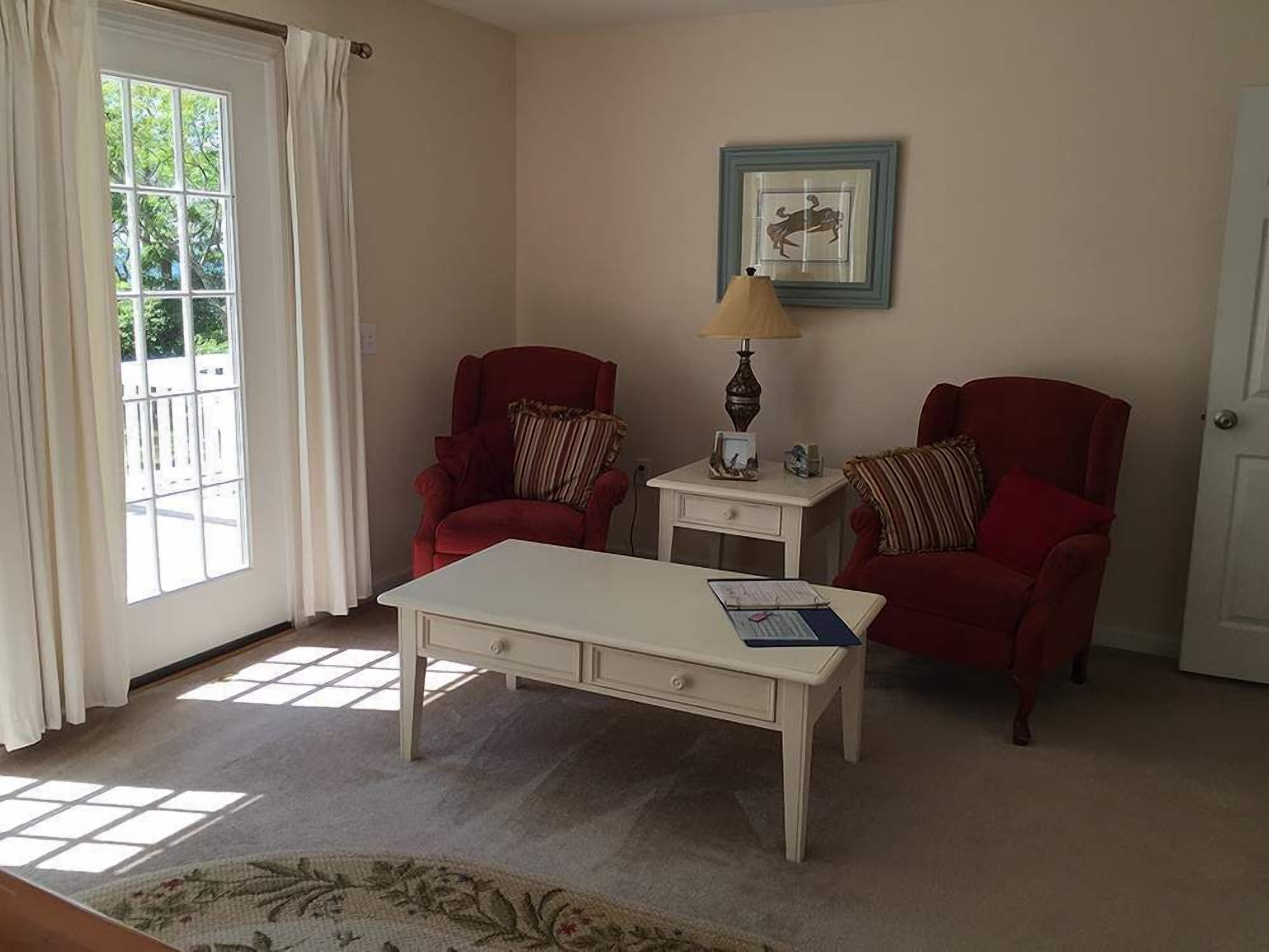 A room with two red armchairs, a white coffee table, a small side table with a lamp, and a framed picture on the wall.