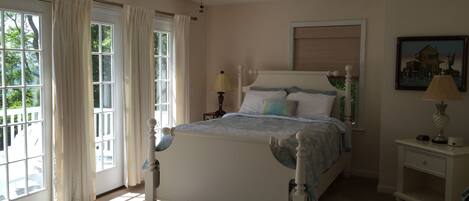 A bedroom with a bed, a ceiling fan, a nightstand, a lamp, and a window with curtains.