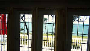 A room with three large windows offering views of the ocean and a white fence. - The Baywood Bed & Breakfast (Cape Charles)