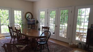A dining area with a round table surrounded by chairs, a rug, and a view through large glass doors. - The Baywood Bed & Breakfast (Cape Charles)