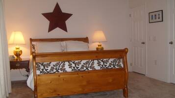 A wooden bed with a decorative headboard, two bedside lamps, a star decoration on the wall, and a door with a framed picture.