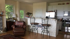 A spacious living area with a fireplace, a large rug, and a leather sofa. There is a kitchen with white cabinets and a stainless steel oven. - The Baywood Bed & Breakfast (Cape Charles)