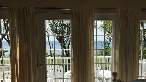 A room with a view of the ocean through a large window, a white door, and a white railing outside. - The Baywood Bed & Breakfast (Cape Charles)