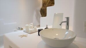 A modern bathroom with a white sink, a large mirror, and a unique wall feature. - Ruby Suite (Mykonos)