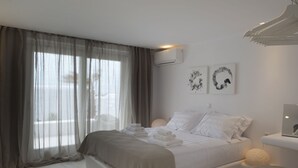 A modern bedroom with a large bed, sheer curtains, and two wall-mounted artworks. - Ruby Suite (Mykonos)