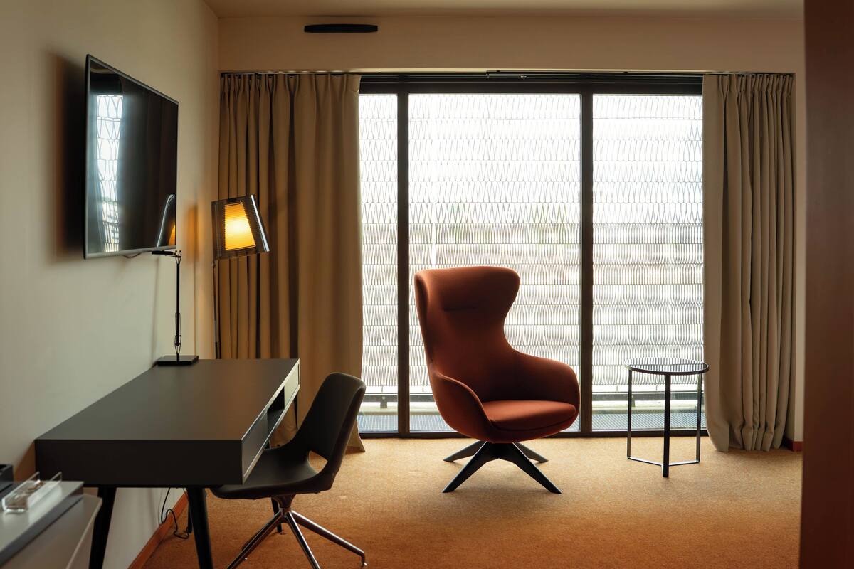 Une chambre d’hôtel avec une grande fenêtre, un téléviseur fixé au mur, un bureau avec une chaise et une petite table.